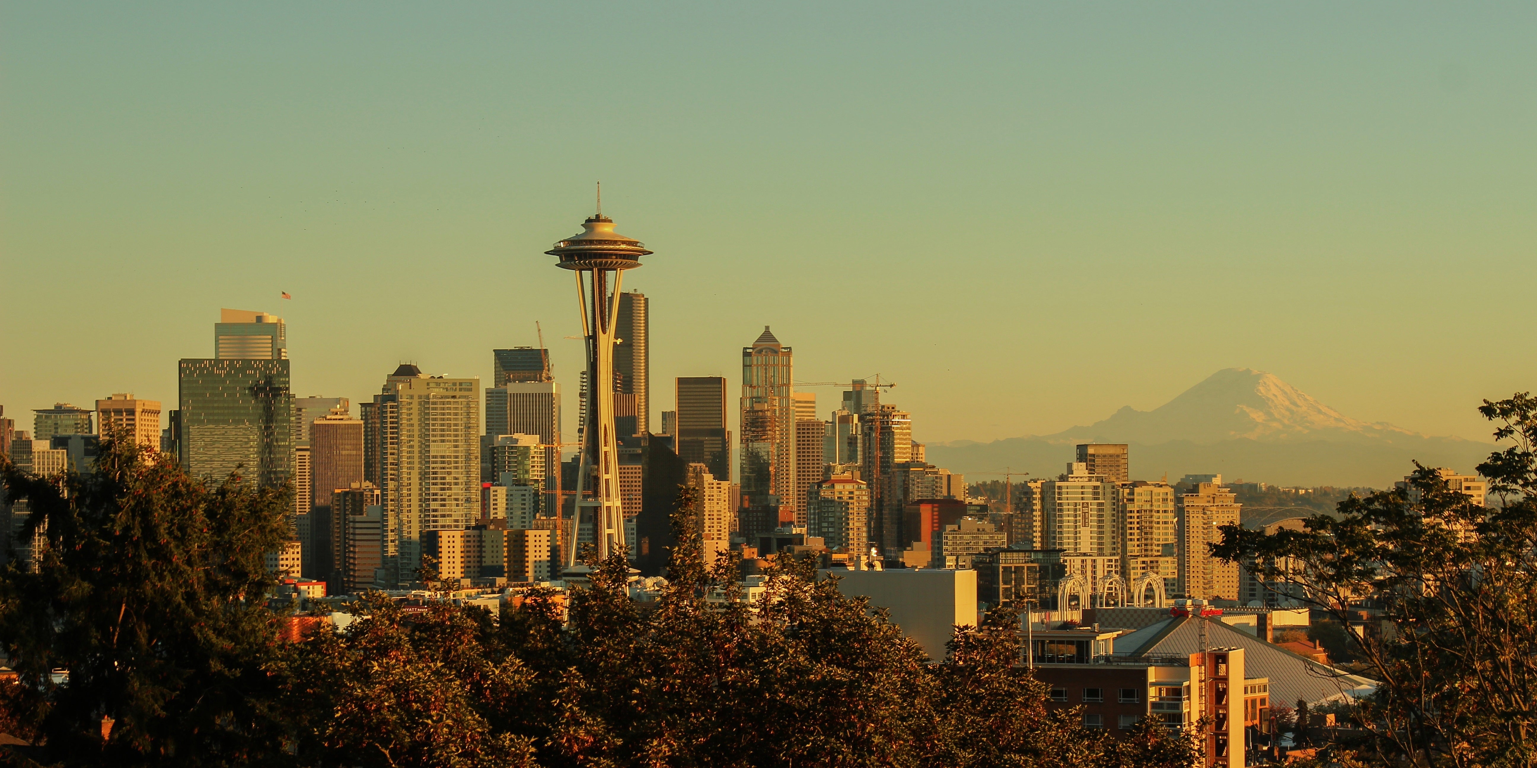 Seattle skyline at sunset with the Space Needle in the foreground and Mount Rainier visible in the distance.