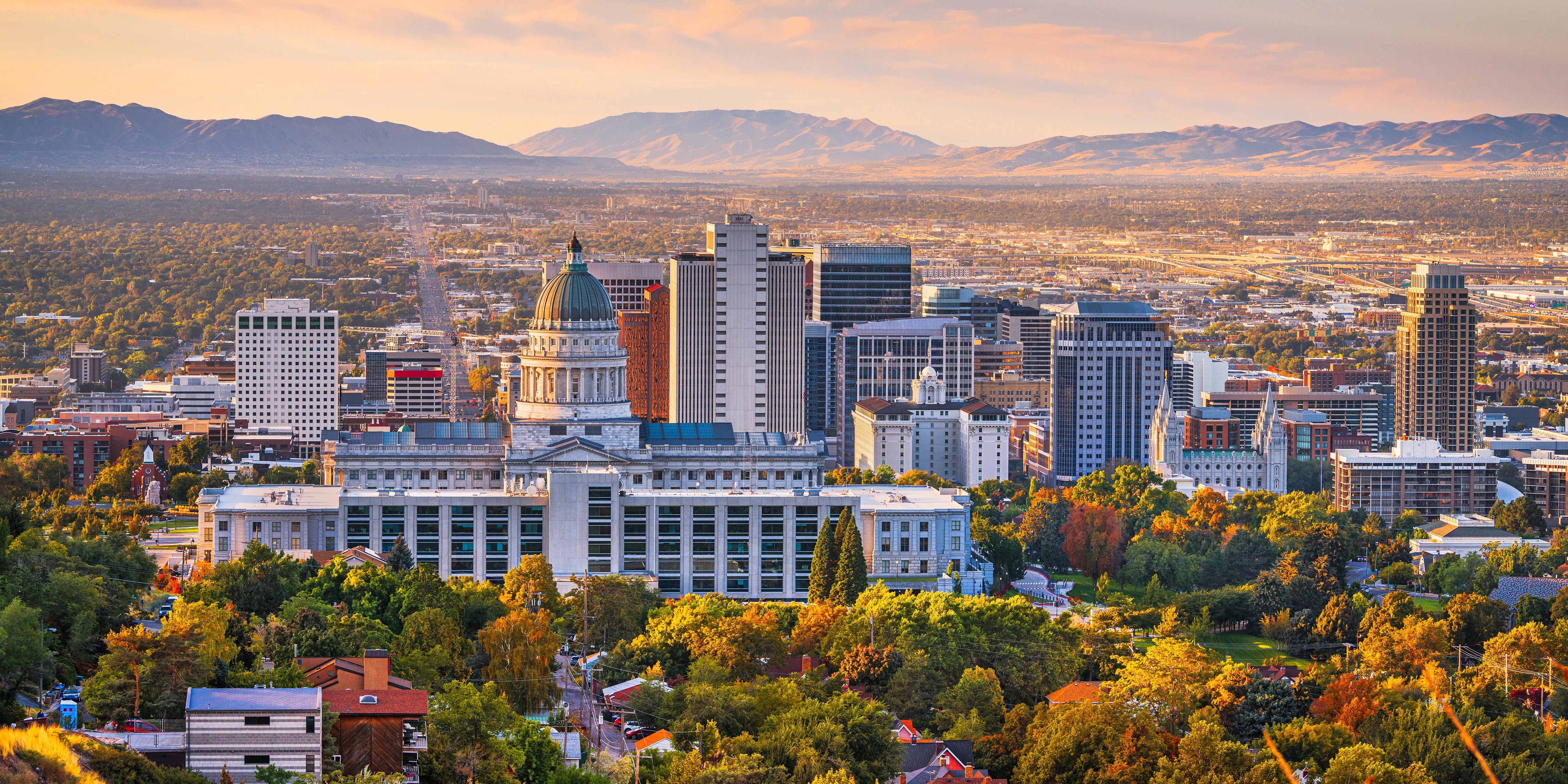 Skyline of downtown Salt Lake City at sunset, with the Utah State Capitol building in the foreground and the Wasatch Mountains in the background.